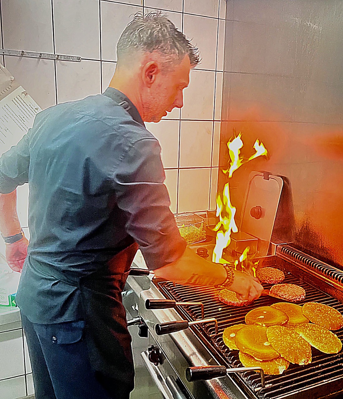 Der Koch des Villa Paul am offenen Holzkohle-Grill, Burger-Patties und Brioche-Buns über der Flamme